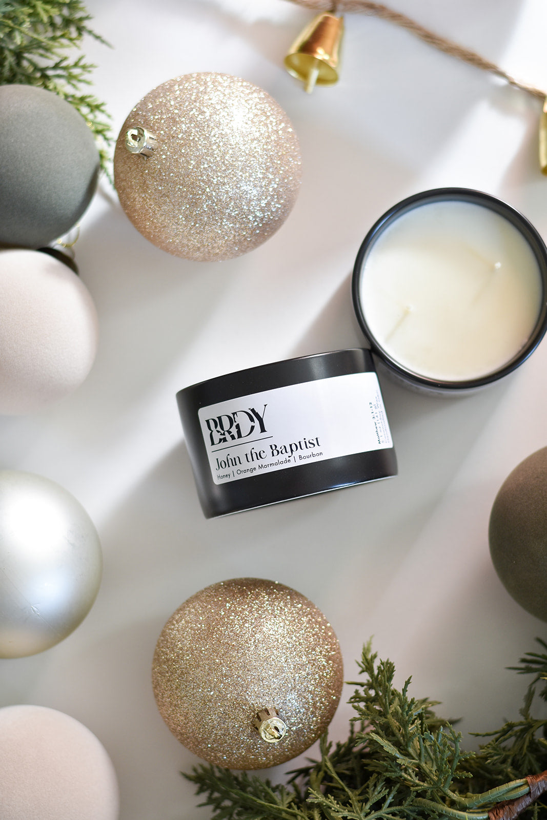 Candle labeled 'John the Baptist' surrounded by decorative ornaments on a light surface.