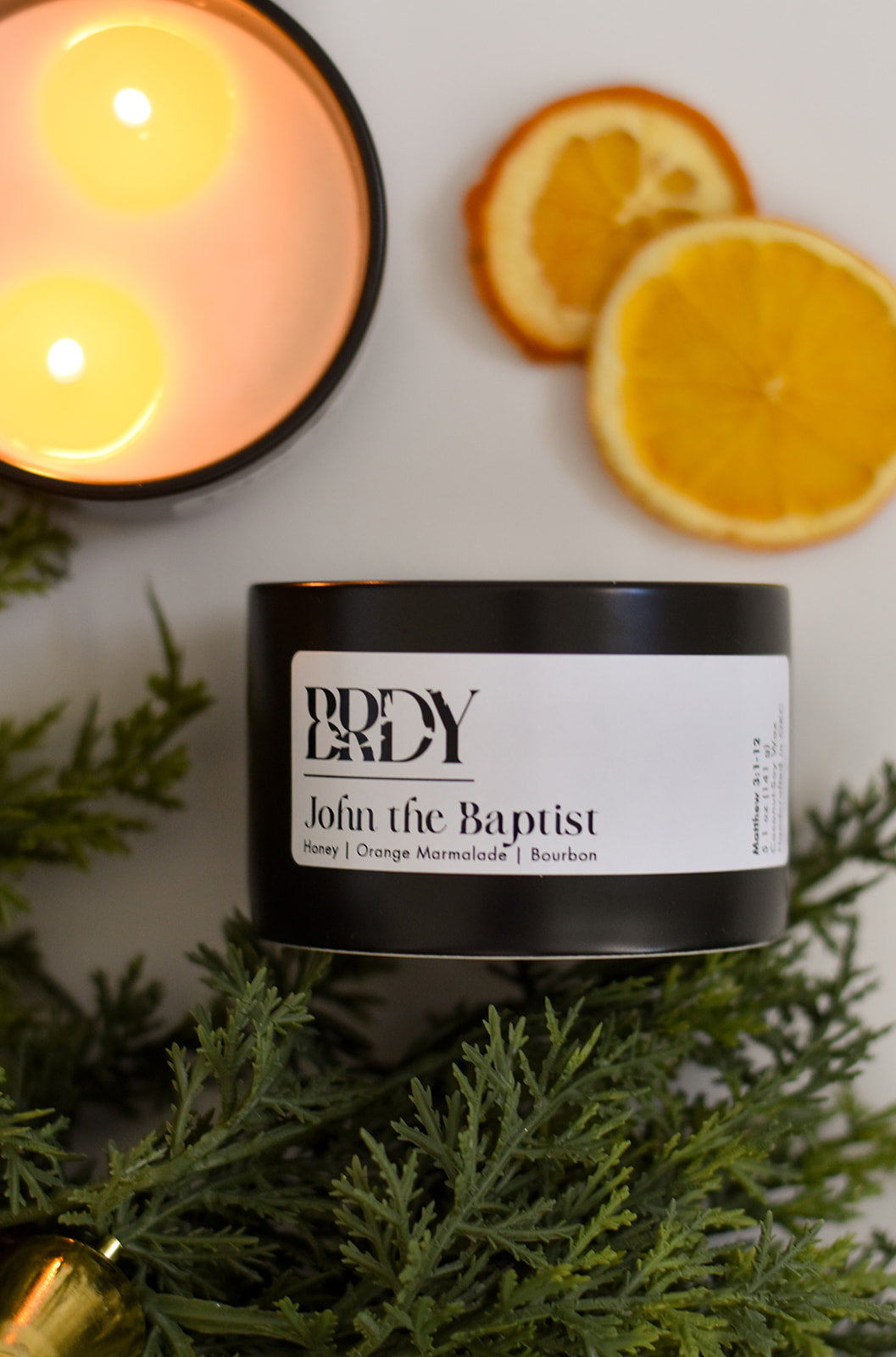 Candle labeled 'John the Baptist' with a lit candle and orange slices in the background